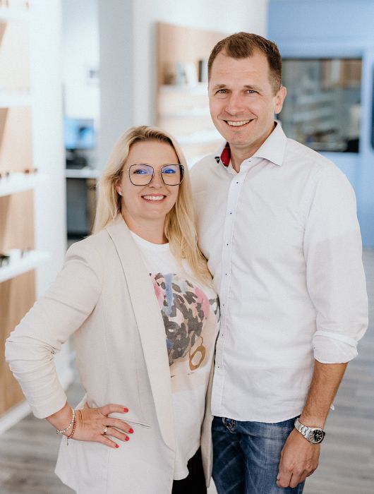 Michael & Sabrina Männing stehen in einem hellen Geschäftsraum nebeneinander und lächeln. (Ausschnitt)